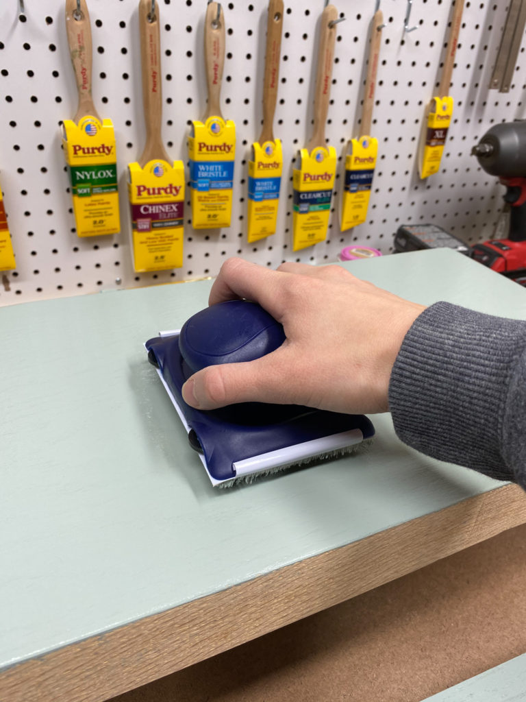 Removing excess solid color stain with a synthetic pad on blue bench