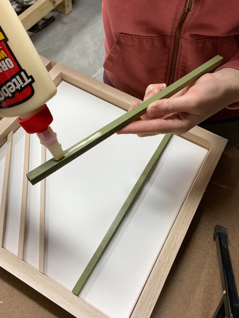 Gluing  wood dowels onto canvases for modern wall art